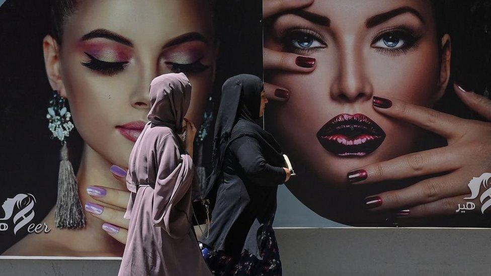 Burqa clad women walk past a billboard put up on the wall of a beauty salon in Kabul on August 7, 2021