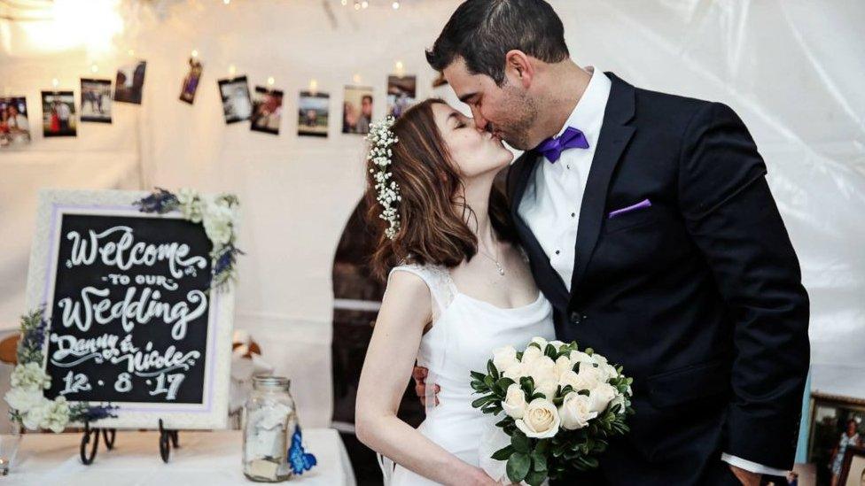 Nicole and Danny, in dress and tuxedo, kiss at their wedding