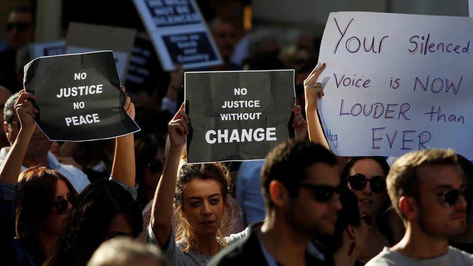 People holding signs that read "No justice no peace," "No Justice without Change," and "Your silenced voice is now louder than ever"