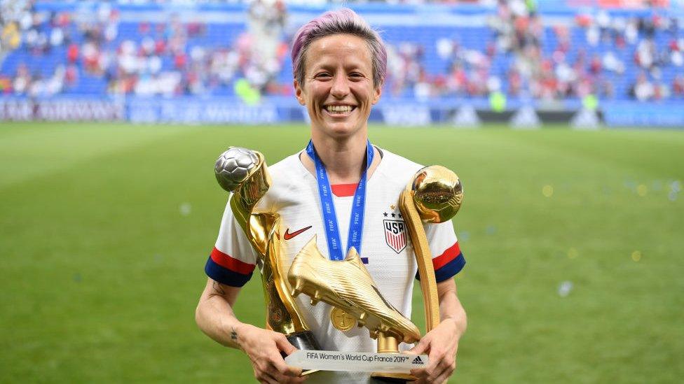 Megan Rapinoe with golden ball, golden boot and world cup trophies.