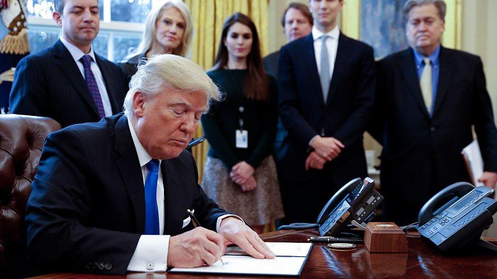 Donald Trump signs an executive order in the Oval Office.