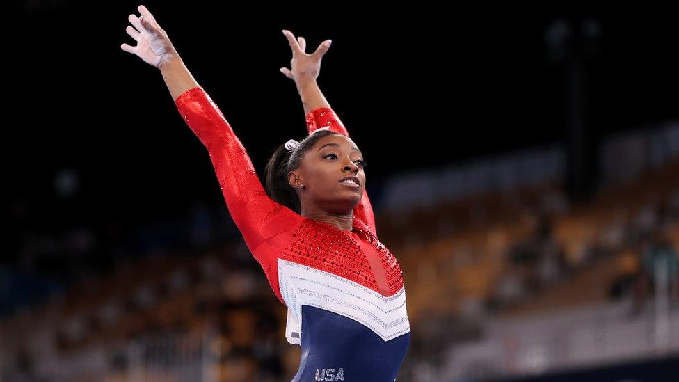 simone biles stood in position ahead of a gymnastic display in front of a large crowd