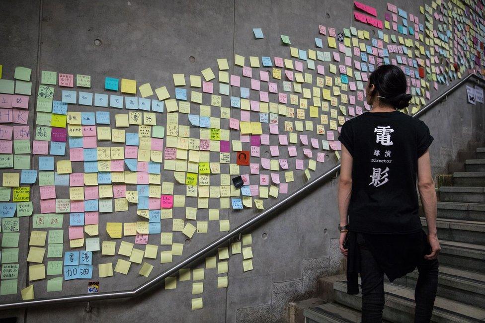 A woman walks past a wall in Hong Kong covered with sticky note messages