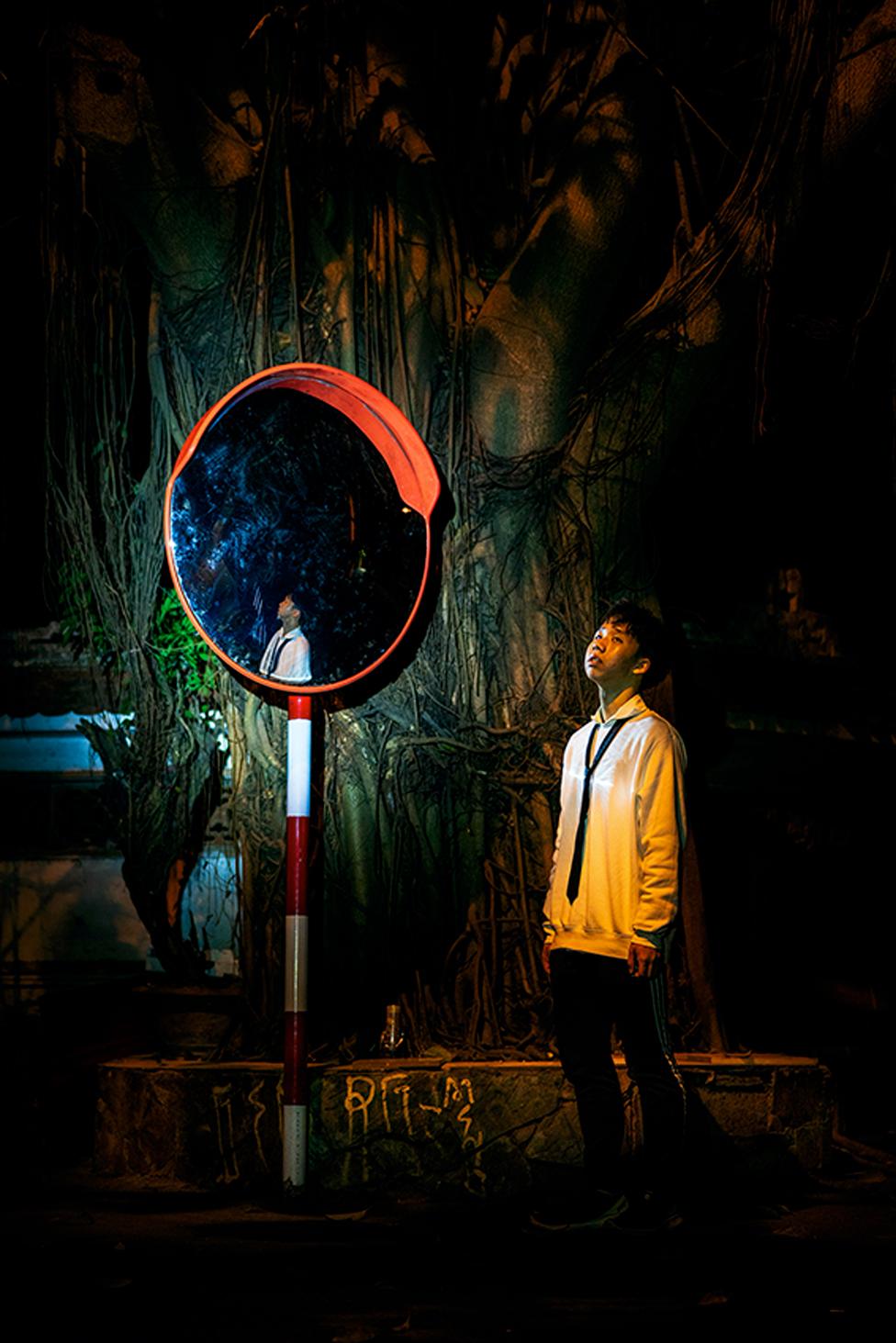 A young man basking in artificial moonlight standing against a derelict background