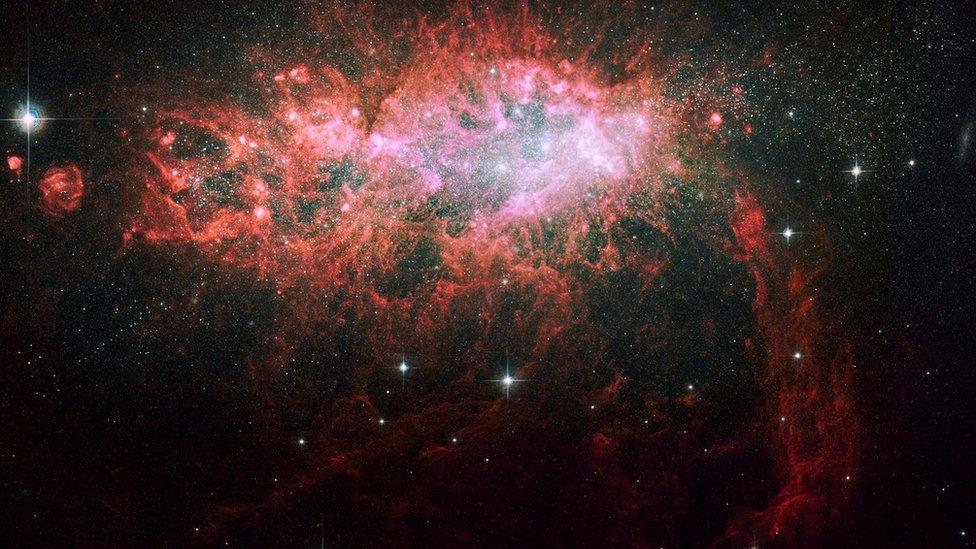 A red and pink dusty cloud with a family of bright stars in the centre