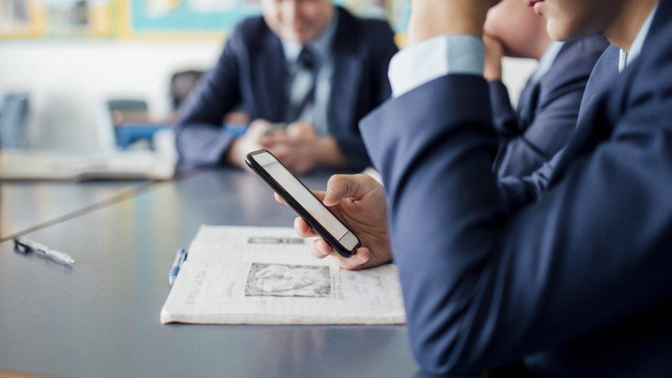 A school pupil in uniform using a smartphone at their desk