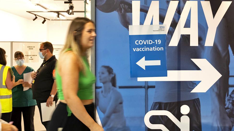 A woman passes a sign directing people to a temporary NHS Covid-19 Vaccination Service site in Trinity Shopping Centre, Leeds, UK, on 8 August 2021