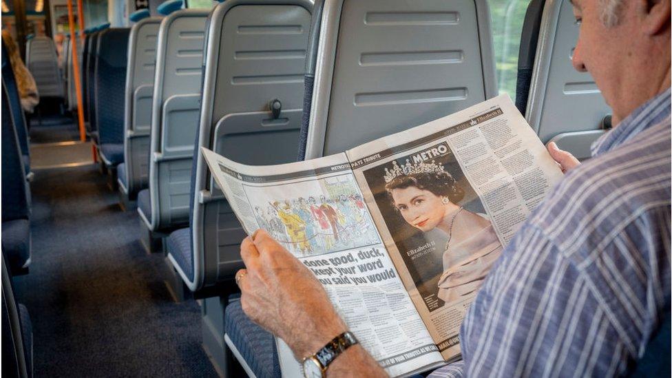 A rail passenger on a train to Windsor reads about the Queen's procession from Balmoral to Edinburgh