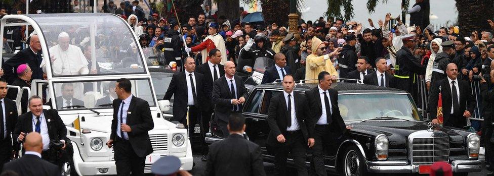 King Mohammed VI (R) waves to the crowd from his car as he arrives with Pope Francis (L) the pontiff's arrival