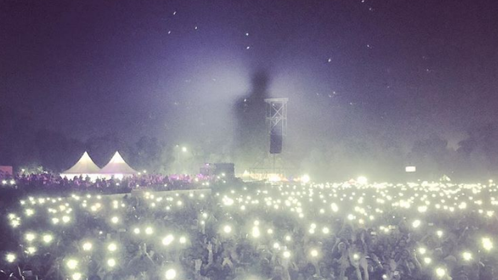 A photograph shows sillouette of singer above growd holding lights