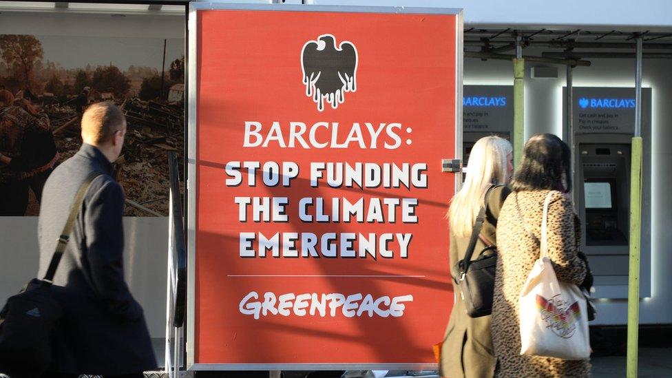 People walk past a Greenpeace protest at a Barclays branch