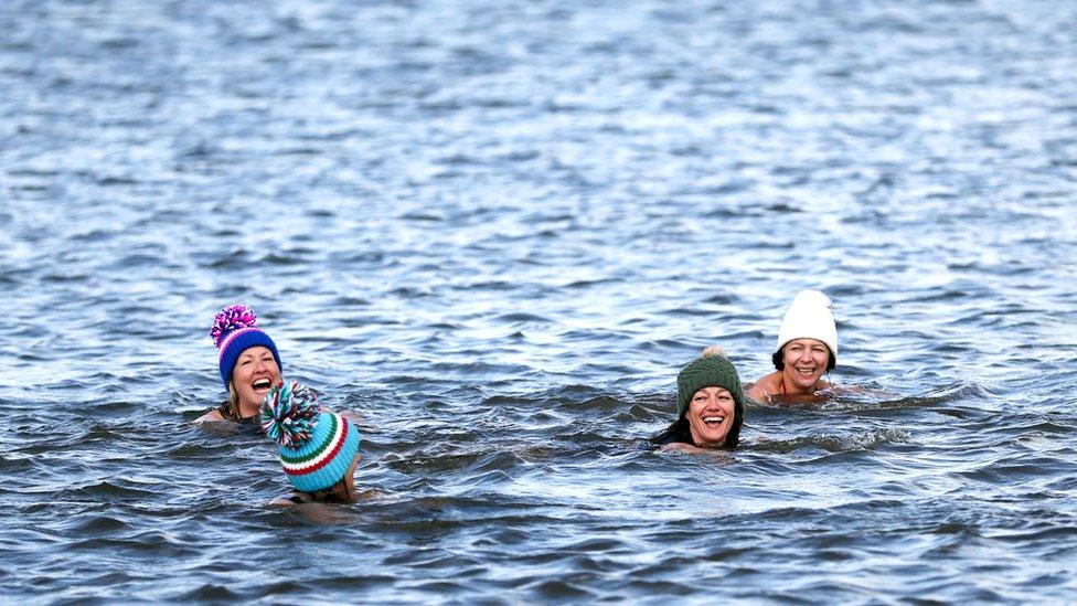 Three confident friends wear woolly hats whilst open water swimming