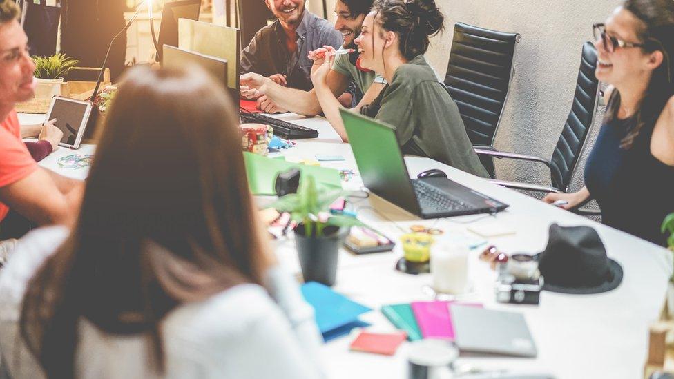 Colleagues around a table talking and laughing at work