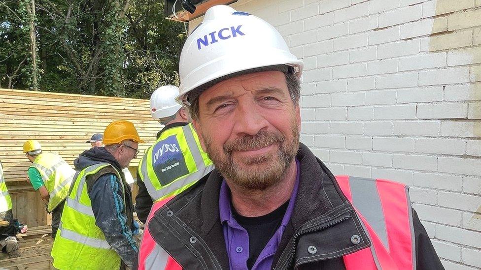 Presenter of DIY SOS Nick Knowles wearing a white hard hat and pink hi-vis vest