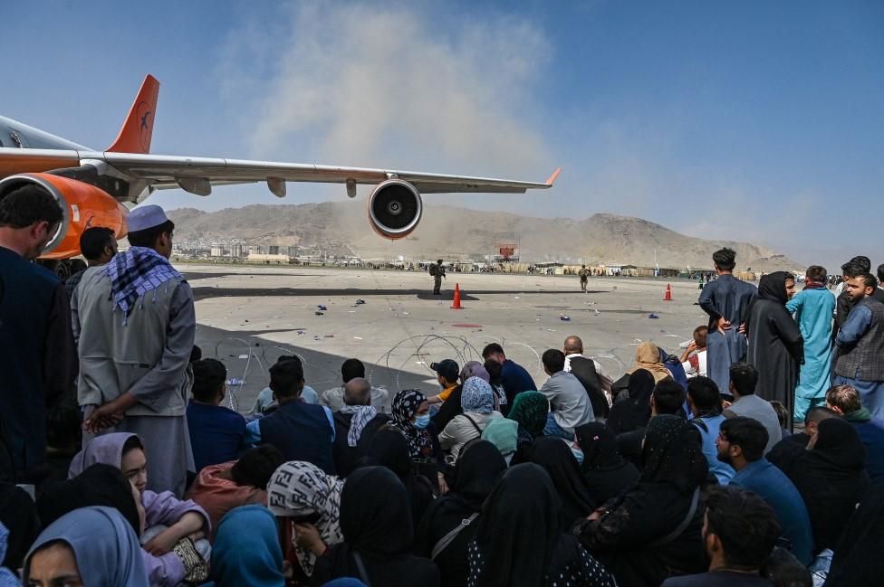 Afghan people sit as they wait to leave the Kabul airport in Kabul on August 16, 2021