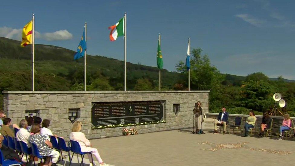 A speech is given in front of a memorial to IRA members, which has an Irish flag on top