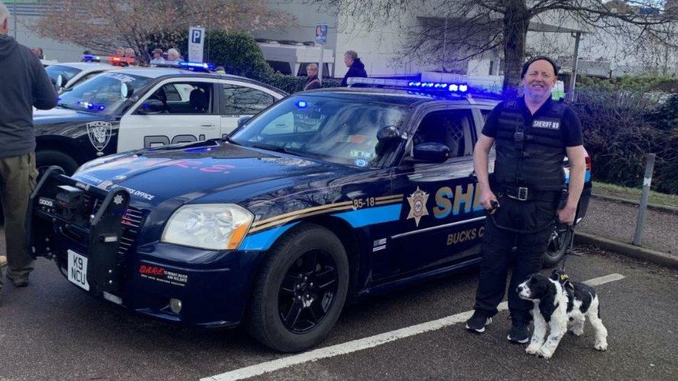 A man and his dog stood next to an American police car