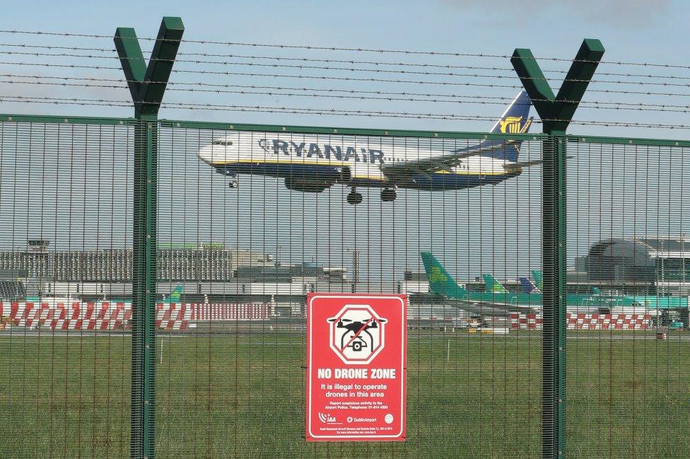 A plane flying into Dublin Airport behind a fence with a sign that reads: No drone zone