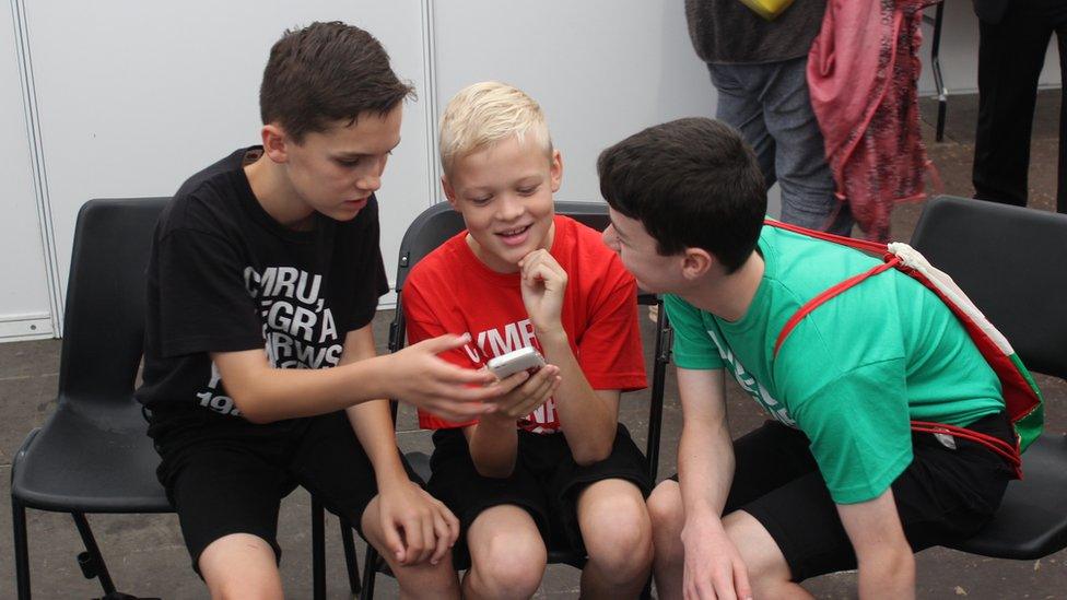 Tri o blant gefn llwyfan yn chwarae gyda ffôn // Three children back-stage playing with a mobile phone