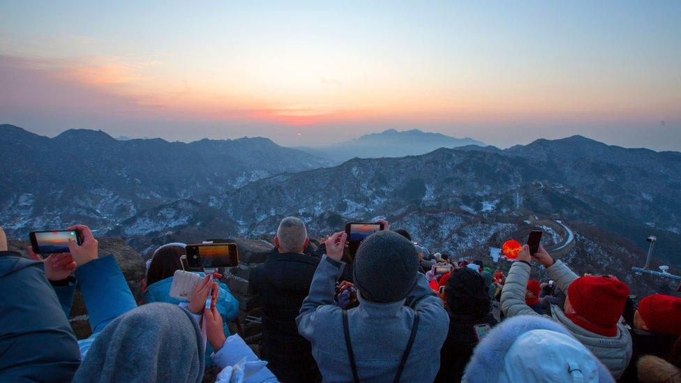 Tourists on the Great Wall take photos of the sunrise with their phone cameras