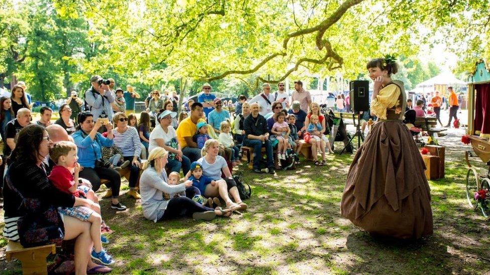 People watch a woman performer, who is smiling at the audience, at Norfolk and Norwich Festival in Chapelfield Gardens in 2018