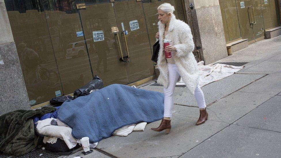 A woman walks past a homeless person sleeping on the street on March 11, 2019 in midtown Manhattan, New York City.