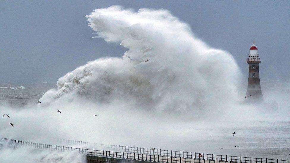 Waves crash against the sea wall and Roker Lighthouse in Sunderland