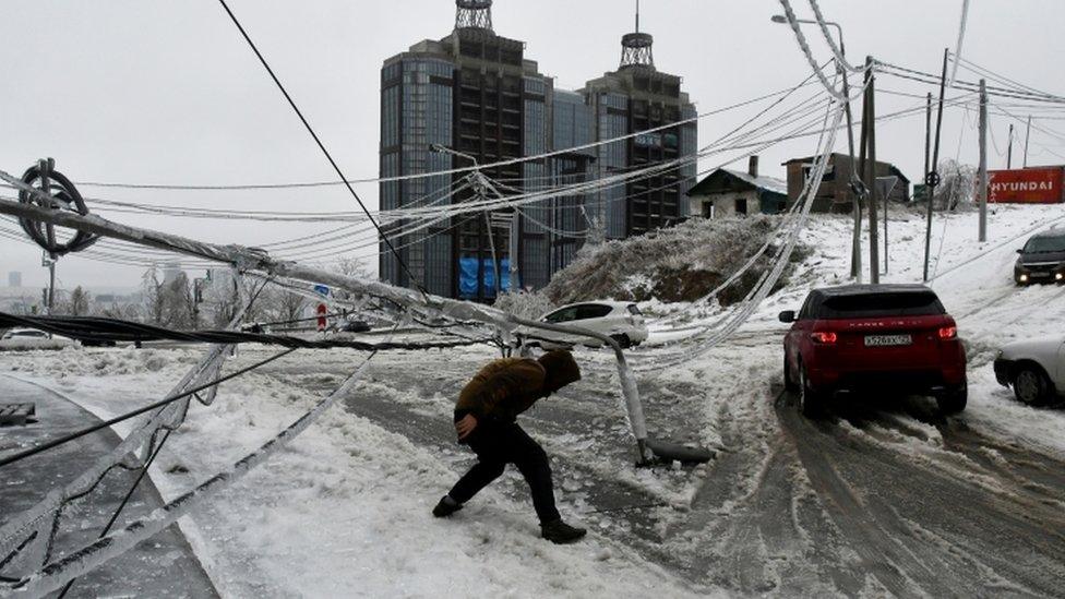 A man walks under a damaged power pole covered with ice after freezing rain in the far eastern city of Vladivostok, Russia