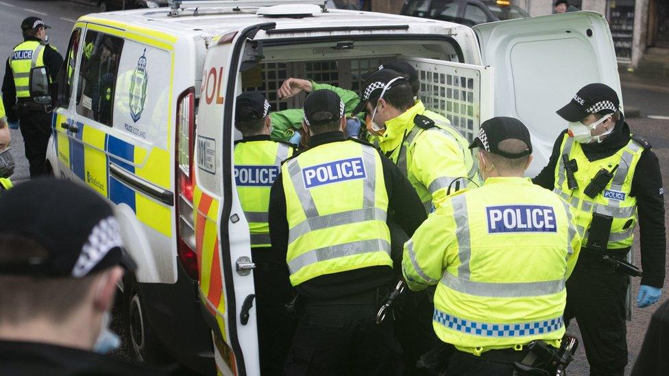 Police handcuff and detain a protester during a Scotland Against Lockdown demonstration outside the Scottish Parliament in Edinburgh