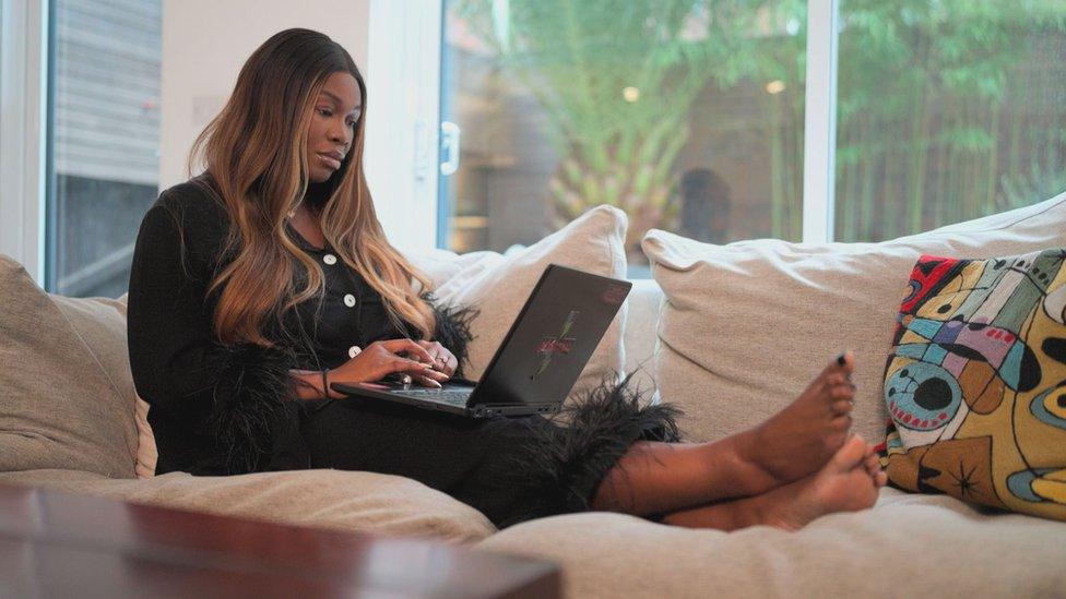 Jackie researching for the documentary, she's lying on a sofa while wearing black fluffy pyjamas