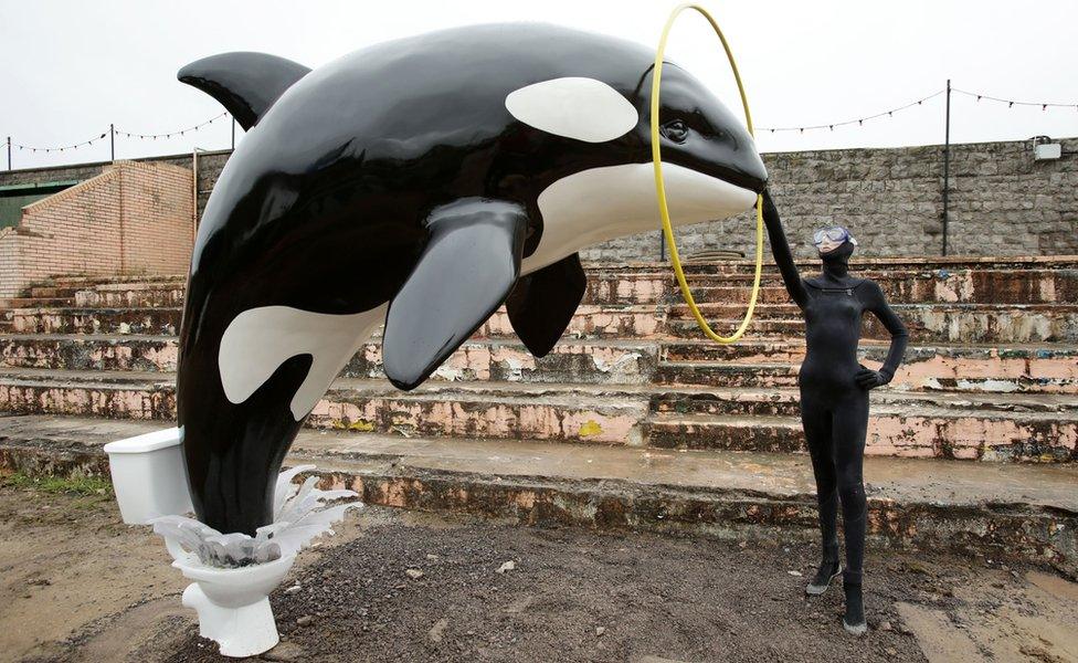 A Banksy piece depicting an orca whale jumping out of a toilet is displayed at Dismaland