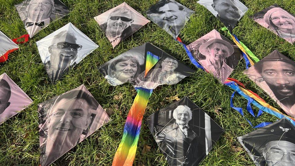 Ascension art, with several kites bearing the faces of people, laid out on grass