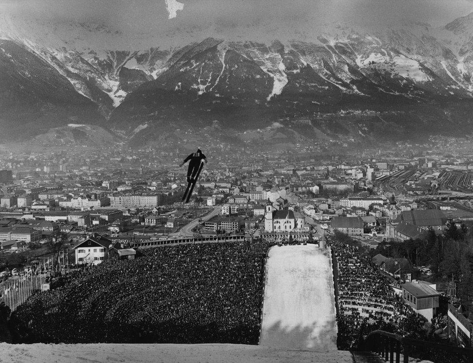 A huge crowd watch a skier suspended in mid-air.