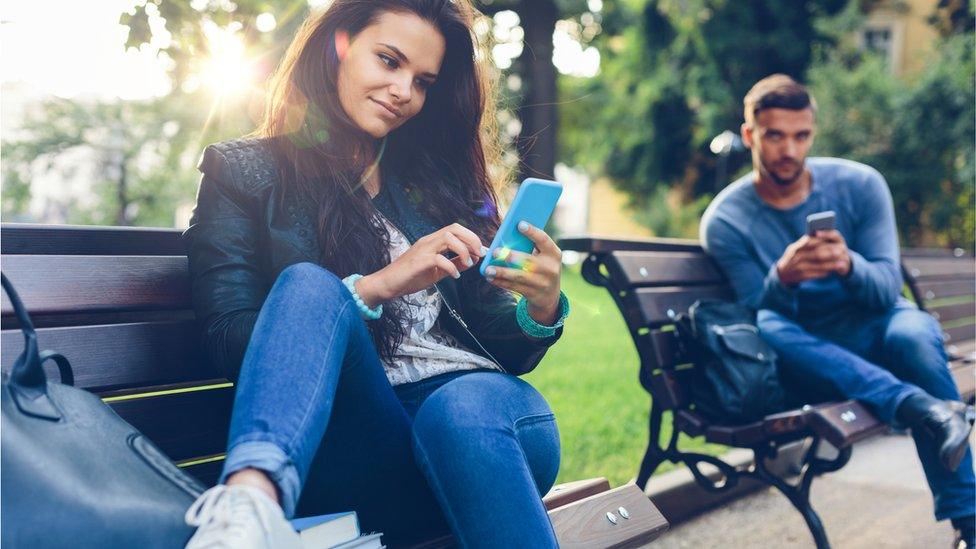 Couple on park benches on smartphones