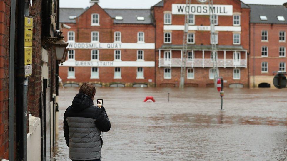 A person looking at their phone in front of flood waters