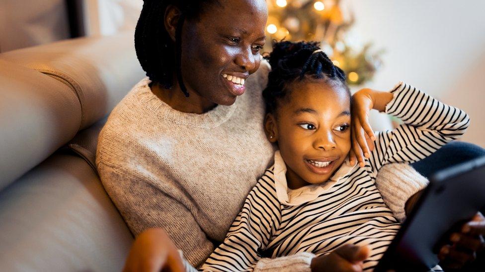 A mum and daughter smile as they look into a tablet together