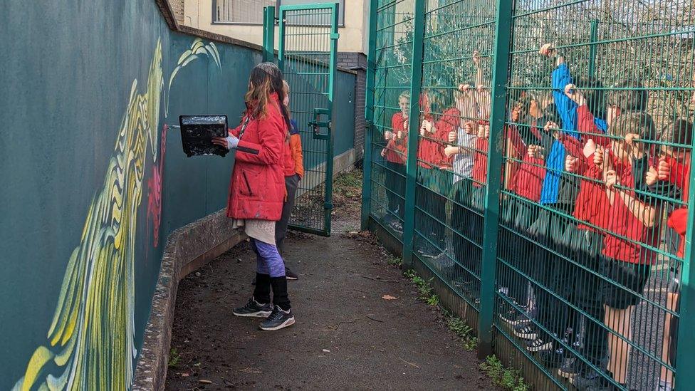 Pupils watching Farrah Fortnam designing on a school building