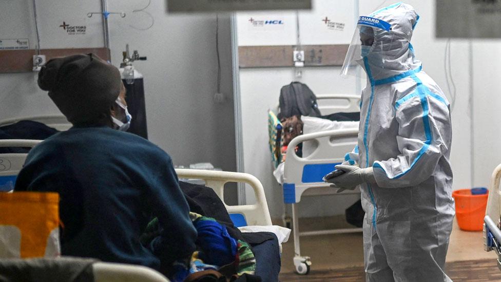 A health worker wearing Personal Protective Equipment (PPE) suit interacts with patients inside a ward at the Commonwealth games (CWG) village sports complex, temporarily converted into Covid-19 coronavirus care centre, in New Delhi on January 5, 2022.