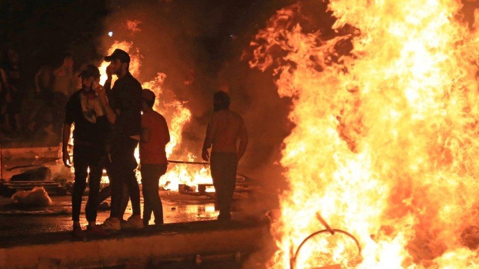 Iraqi protesters burn items to block a road during clashes with security forces