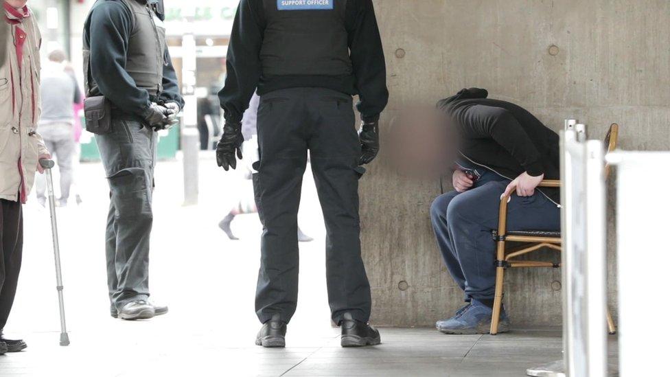 PCSOs with a man sat bent over in chair on street