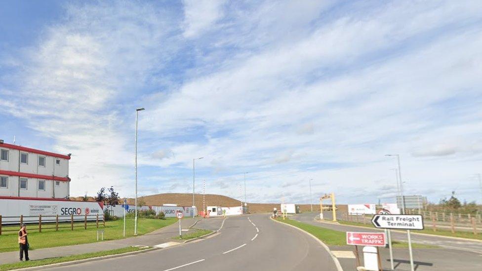 Entrance to rail freight terminal, showing road signs and temporary site buildings