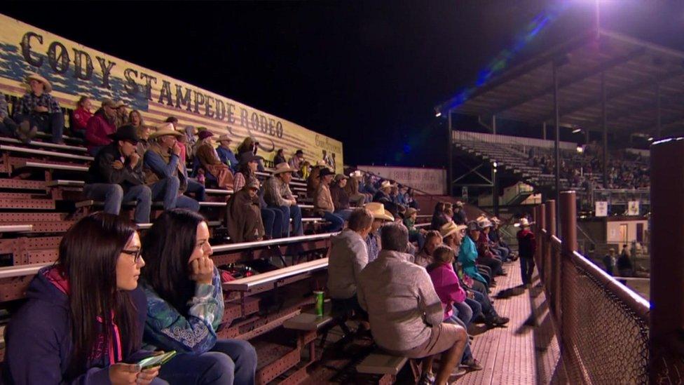 Spectators at rodeo sit on benches