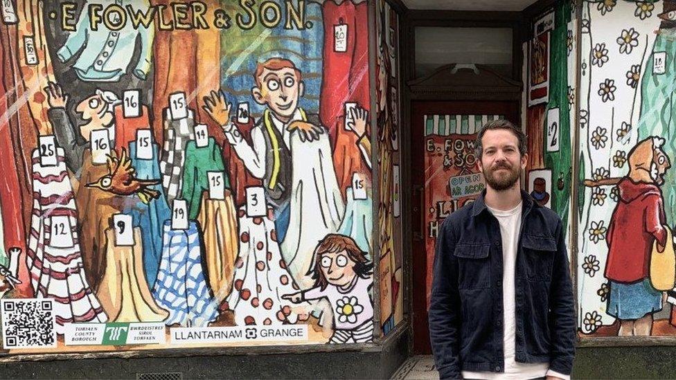 Illustrator Jack Skivens smiles outside E Fowler & Son - the location of his first commissioned piece