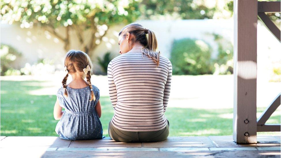 A woman and girl sit facing away together