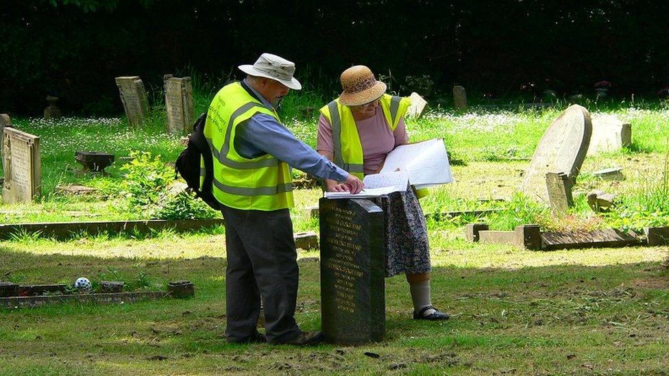 Two people standing by a gravestone