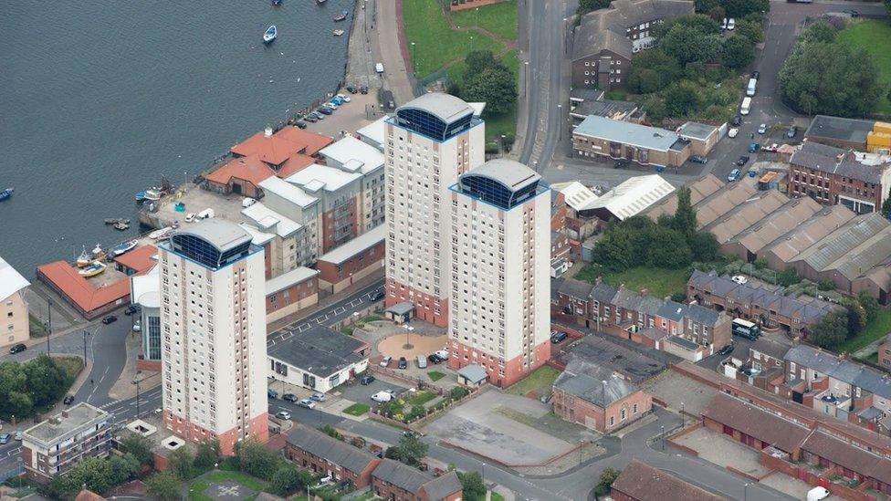 Aerial view of hall surrounded by rows of houses and three tower blocks