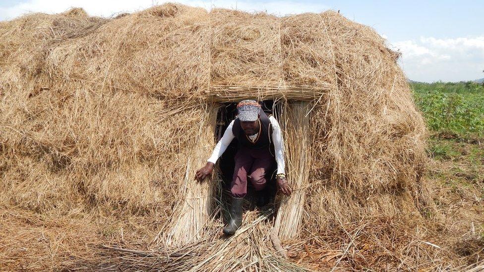 Man coming out of grass house