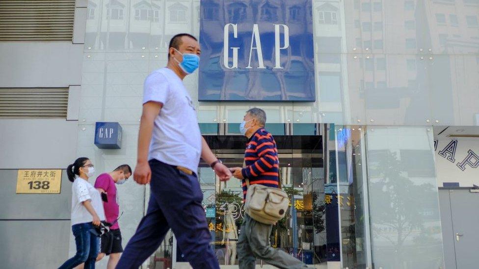 Customers walk outside a GAP store with protective masks in Beijing, China.