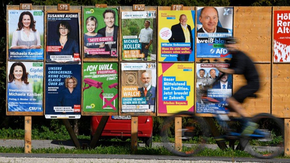 A cyclist rides past several election campaign posters in Bad Feilnbach, Germany on 6 October 2018