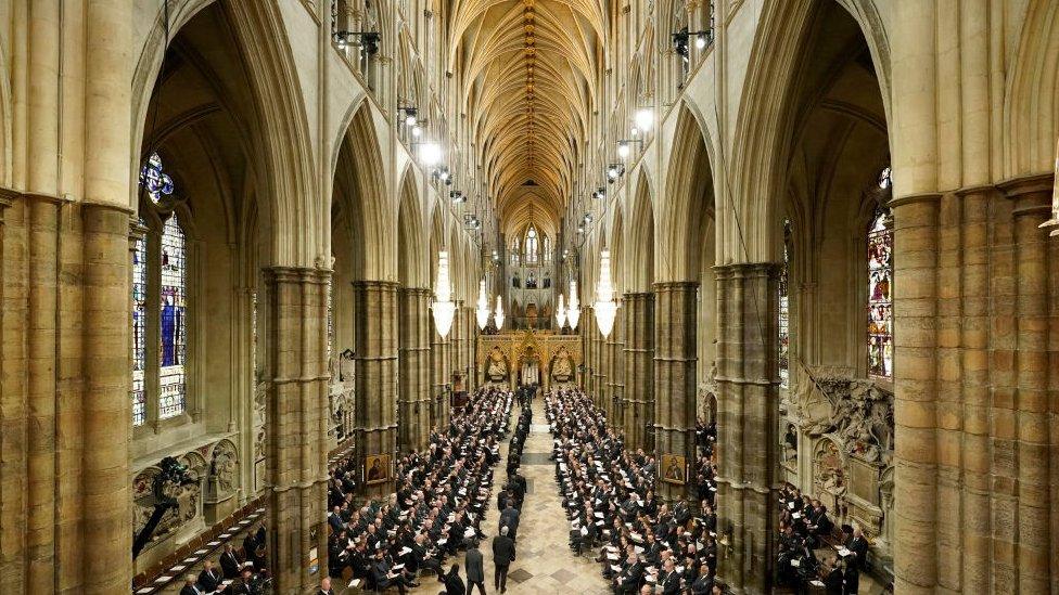 Westminster Abbey, with guests in black and white queueing up and sitting down.